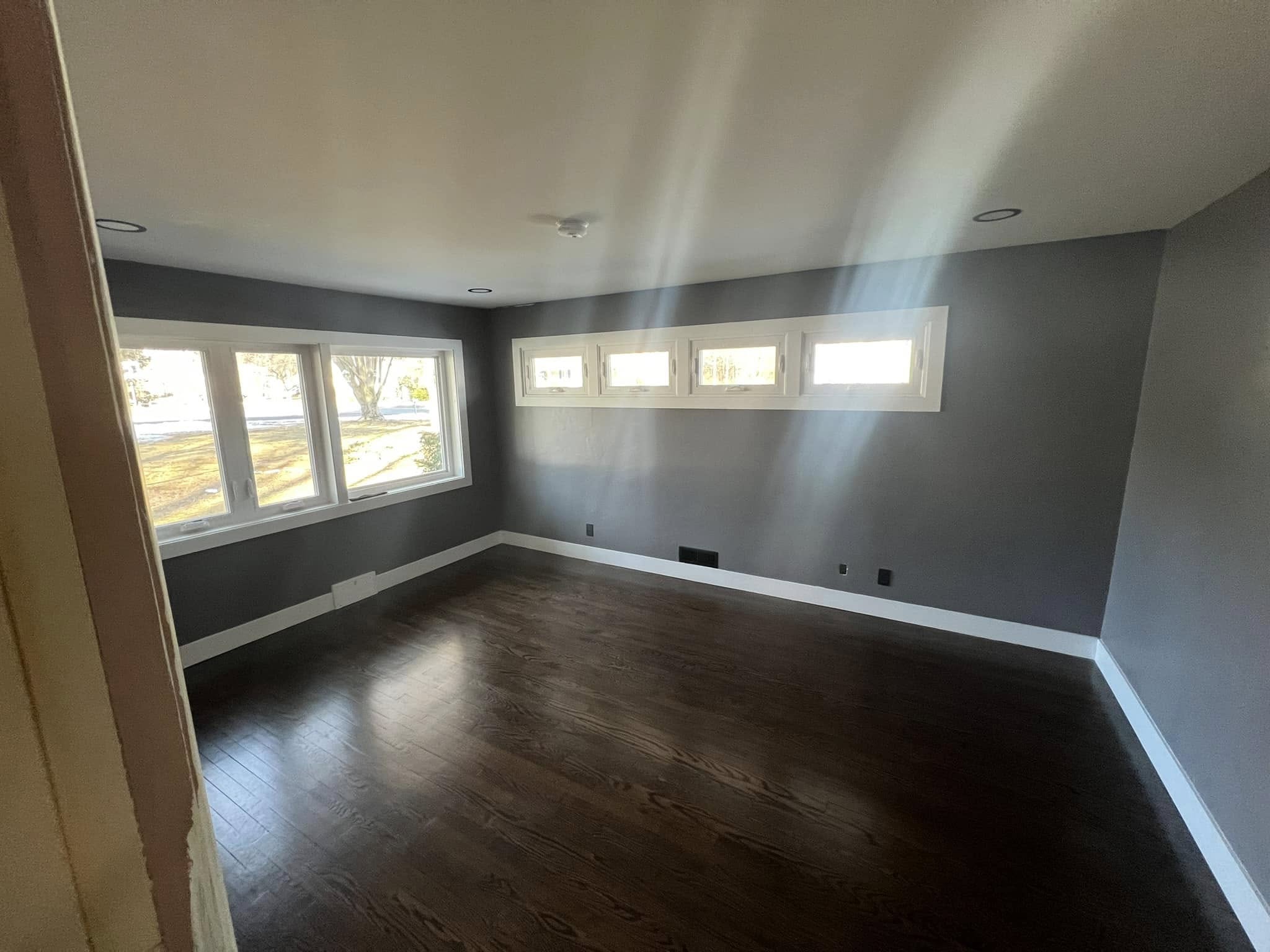 addition with wood flooring windsor connecticut Freshly added room with dark hardwood flooring, smooth gray walls, and bright white trim. Features a row of large windows on one wall and smaller rectangular transom windows on another, allowing natural light to fill the space. Located in Windsor, Connecticut.